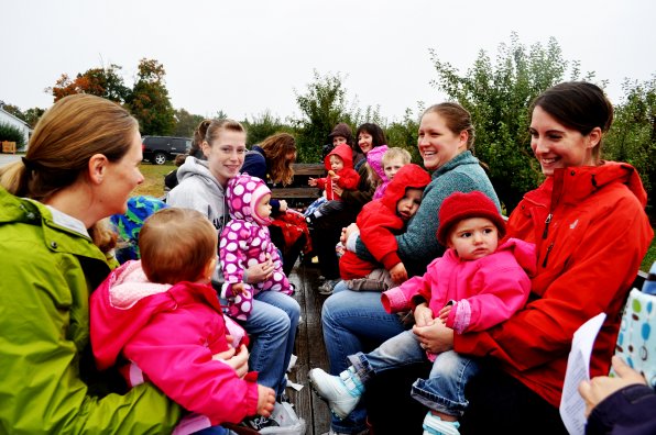 How many moms can you fit in an orchard wagon? This many! MOMS Club President Kristen Johnson (far left) and Vice President Sarah Valle (far right) lead a group into the apples.