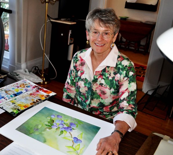 Mary Ruedig at her desk with another watercolorful painting.
