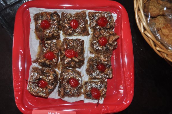 A tray of delectable pecn bars with cherries.