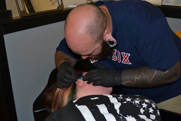 Master Foosh attempts to rewire the brain of tattoo manager Kristy Case by pretending to pierce her ear.