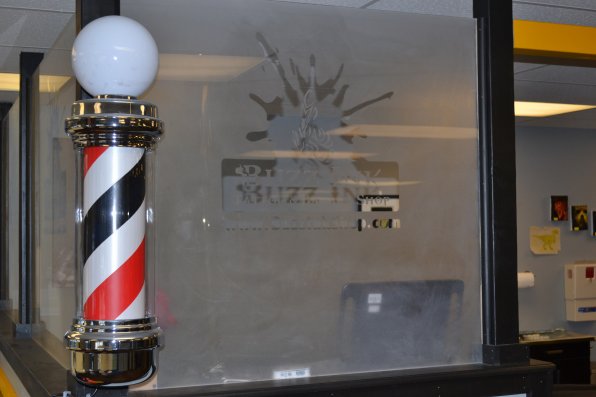 A classic barbershop pole is flanked by frosted glass with the business’s logo.