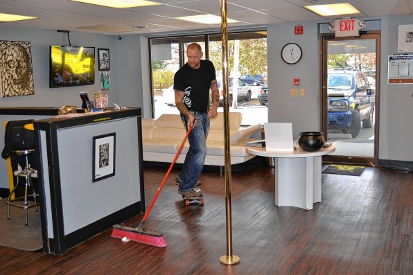 What’s that? Oh, it’s just Rick Broider sweeping. On a skateboard. Next to the dancing pole. In the middle of Buzz Ink, his tattoo, barber and piercing shop.