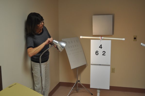 Denise Caruso illuminates an eye chart used when first meeting with clients. Charts are often stationed only 10 feet away from clients, rather than the customary 20 feet.