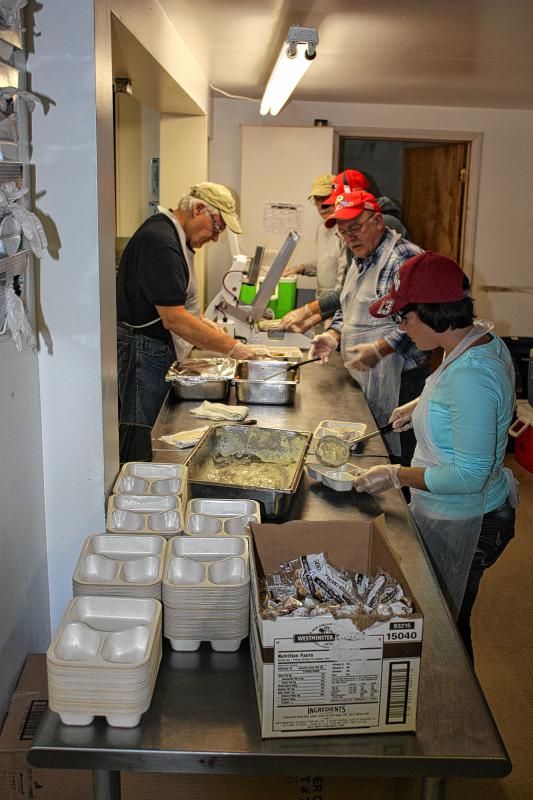 Amy Prickett (right) scoops a serving of fish chowder into a meal tray while others work to fill, wrap and package the trays at the Community Action Program Belknap-Merrimack Counties center in Concord. (JON BODELL / Insider staff) - 
