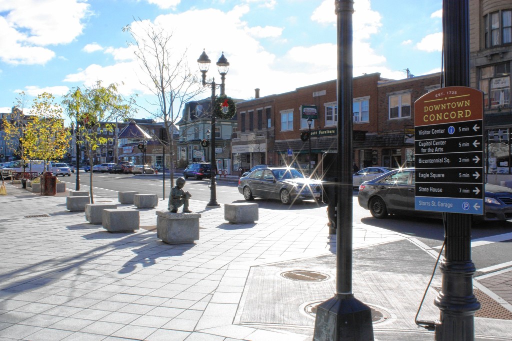 There's an absolute slew of new South Main Street stuff in this photo.  In the foreground there's a new direction-giving sign and a new light post. Behind those are new granite blocks for seating and a new statue of a boy holding a turtle, with new trees and a new trash barrel behind  them.