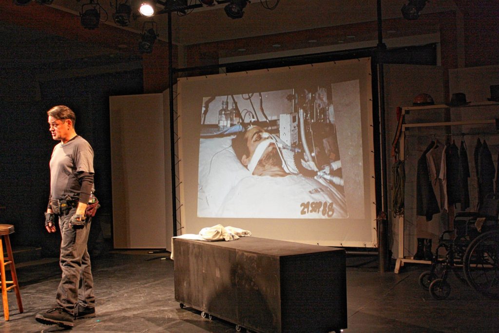 Alan Wilbar performs his one-man-show, The Learning Man, at Hatbox Theatre last Friday night. Behind him is an image of him in the hospital after he suffered a 47-foot fall in 1988.