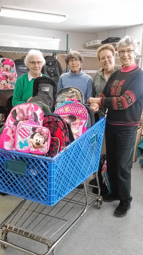 From left: RSVP volunteers Marge Pratt, Mickey Russo, Kathy Bush and Fran Philippe stand next to a shopping cart full of filled backpacks -- the first load of the Merrimack Valley School District Backpack Program at the end of February vacation earlier this year. (Courtesy of Jennifer Army, The Friends Program)