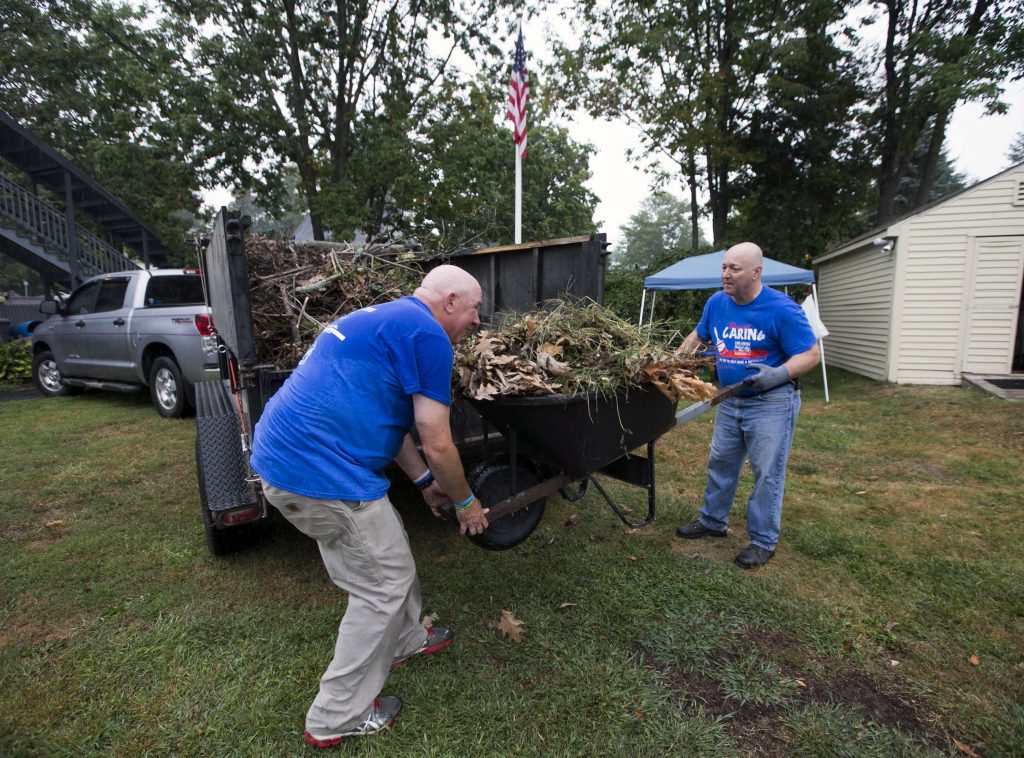 Merrimack County sheriffs Paul Montray, left, and Mario Messna empty out a wheelbarrow full of weeds at the Penacook Community Center on the United Way Day of Caring Wednesday. GEOFF FORESTER