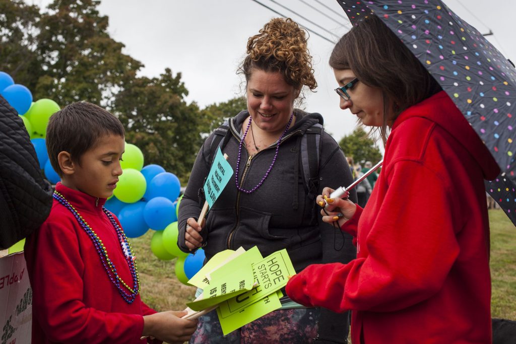 Brita Tirrell (center) and Emily Weber, both of Concord, pick out signs to hold from Keegan Bennett, 10, before joining walkers during NAMIWalks NH on Sunday in Concord, Oct. 2, 2016. (ELIZABETH FRANTZ / Monitor staff) ELIZABETH FRANTZ