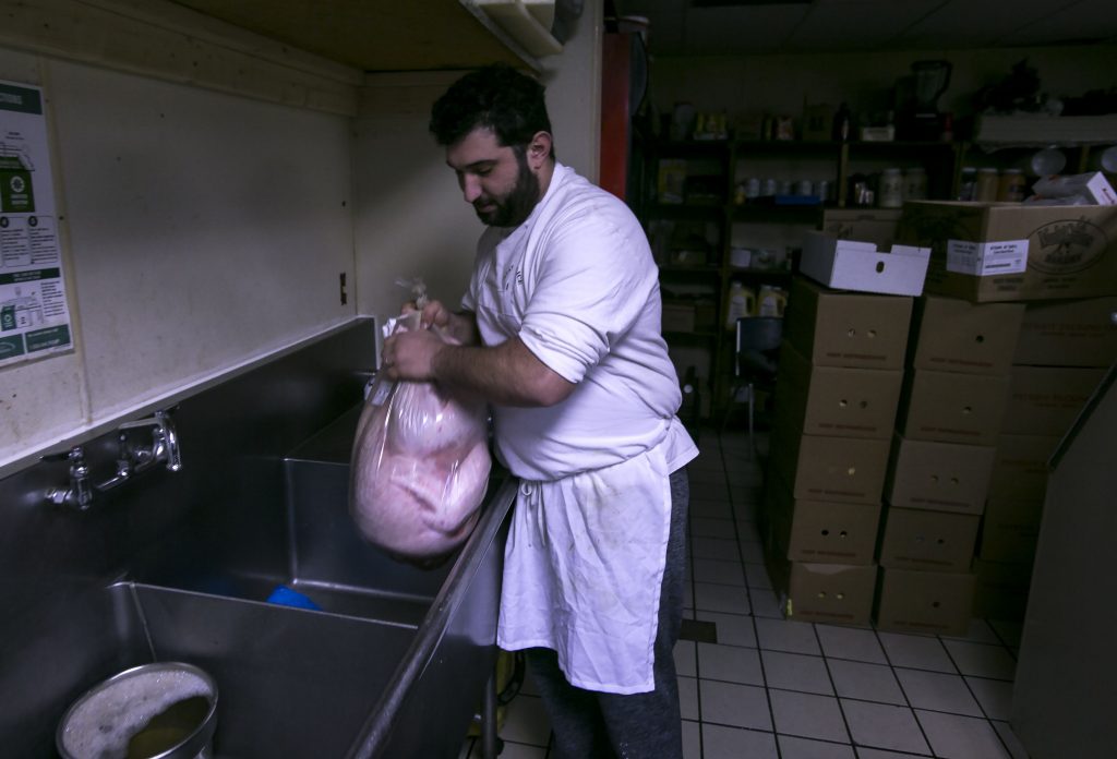 Kosmas Smirnioudis lifts up a 45 pound turkey that is ready to be cooked in preparation of the annual Windmill Family Restaurant Thanksgiving dinner on Thursday. Smirnioudis’ father started the tradition in 1990 when he paired up with the Friendly Kitchen in offering dinners on Thanksgiving.  GEOFF FORESTER