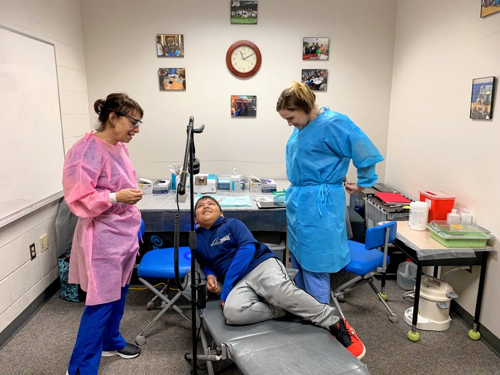 Certified Public Health Hygienist Mary Davis (left) and Dental Assistant Brittani Oldham comfort second-grader Anurag Das (center) before he recieves dental treatment Wednesday at Penacook Elementary School. 