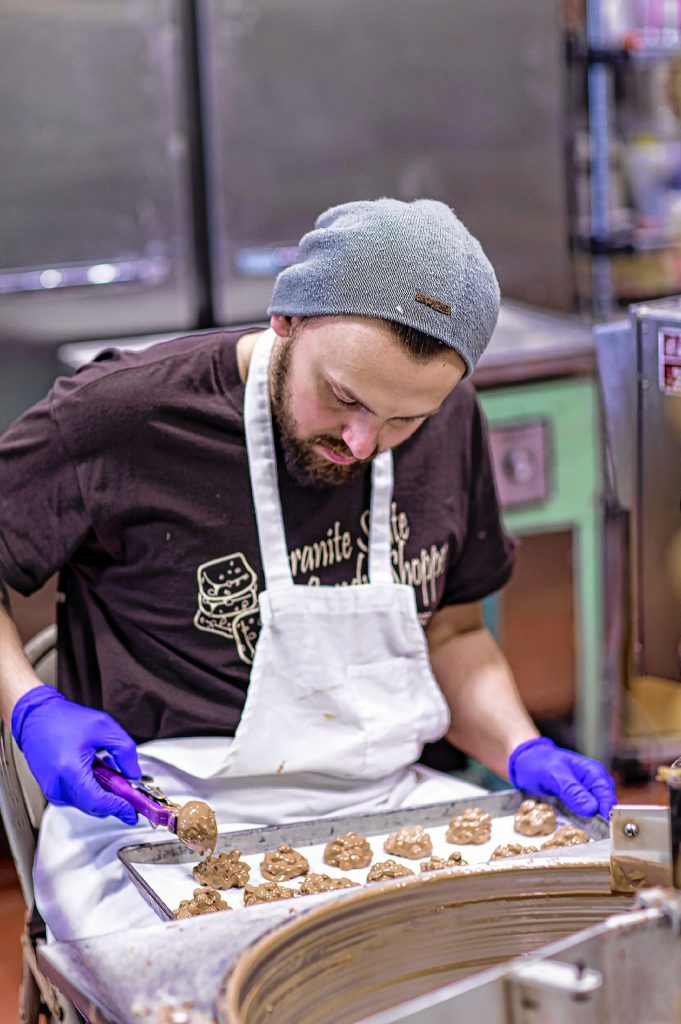 Chocolatier Joe LaFond of Granite State Candy scoops out peanut milk chocolate clusters on Thursday, December 12, 2109 at the Warren Street store. GEOFF FORESTER