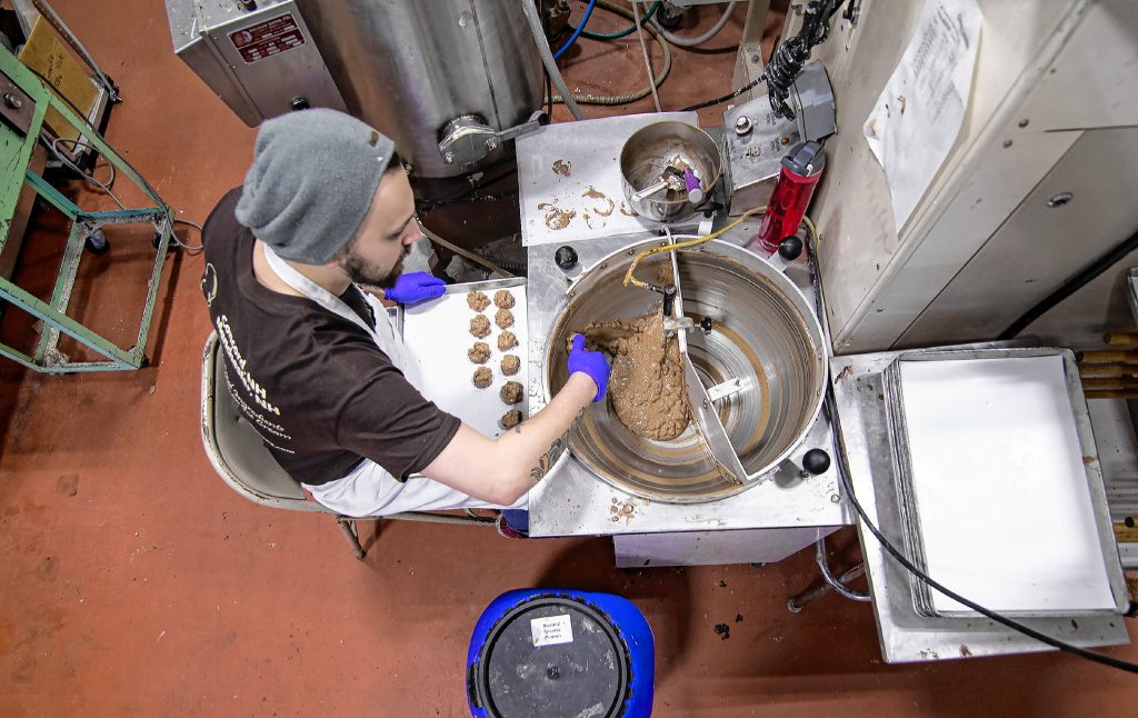 Chocolatier Joe LaFond of Granite State Candy scoops out peanut milk chocolate clusters on Thursday, December 12, 2109 at the Warren Street store. GEOFF FORESTER