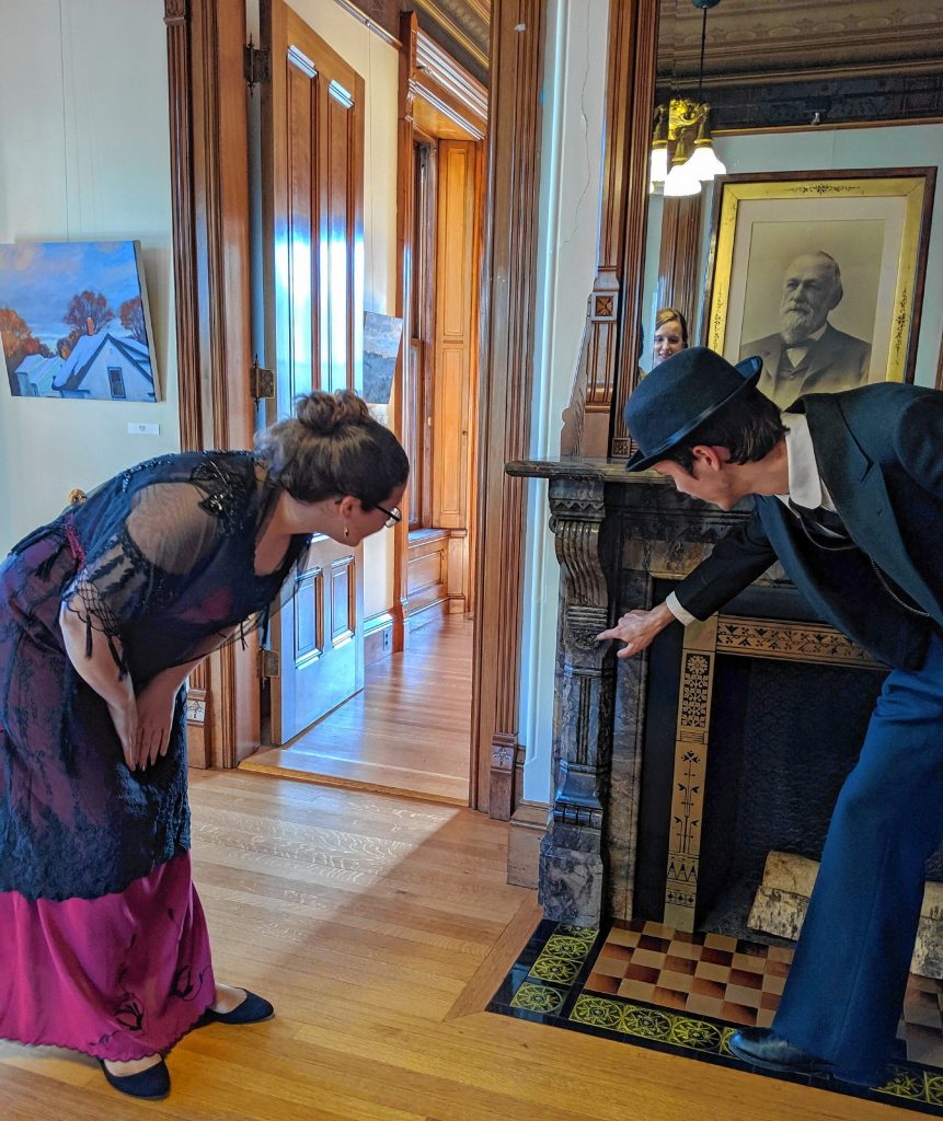 Clark Todd, as architect Amos Cutting, points to details of the fireplace mantle to Eleanor Poirier, appearing as Louise Kimball Jenkins.  