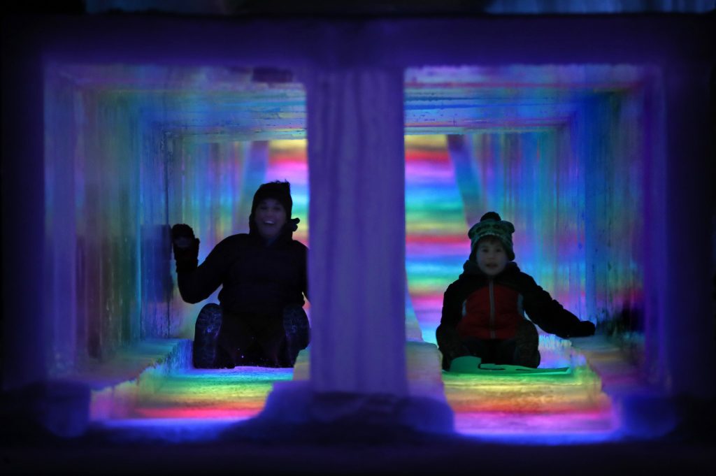 In this Friday, Jan. 25, 2019 photo, visitors race down the side-by-side tunnels of a 97-foot ice slide at Ice Castles in North Woodstock, N.H. The winter wonderland is one of six in North America. (AP Photo/Robert F. Bukaty)  Robert F. Bukaty