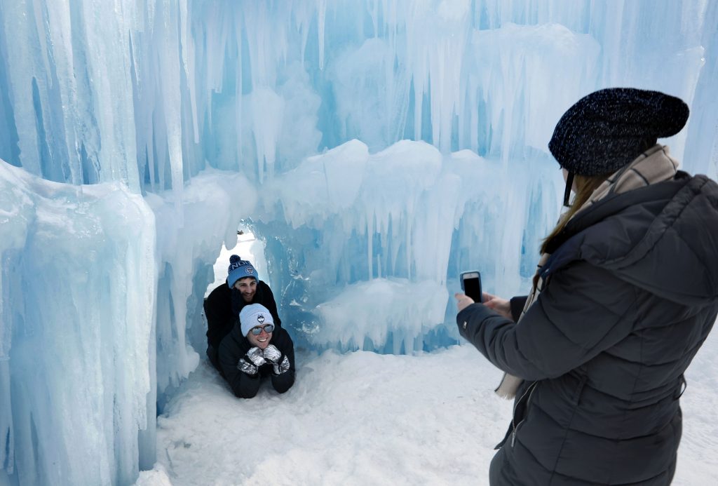 In this Saturday, Jan. 26, 2019 photo, visitors pose for a photo in a tunnel at Ice Castles in North Woodstock, N.H. With a seemingly endless variety of photo-ops, most visitors have a hard time putting their cameras down. (AP Photo/Robert F. Bukaty)  Robert F. Bukaty