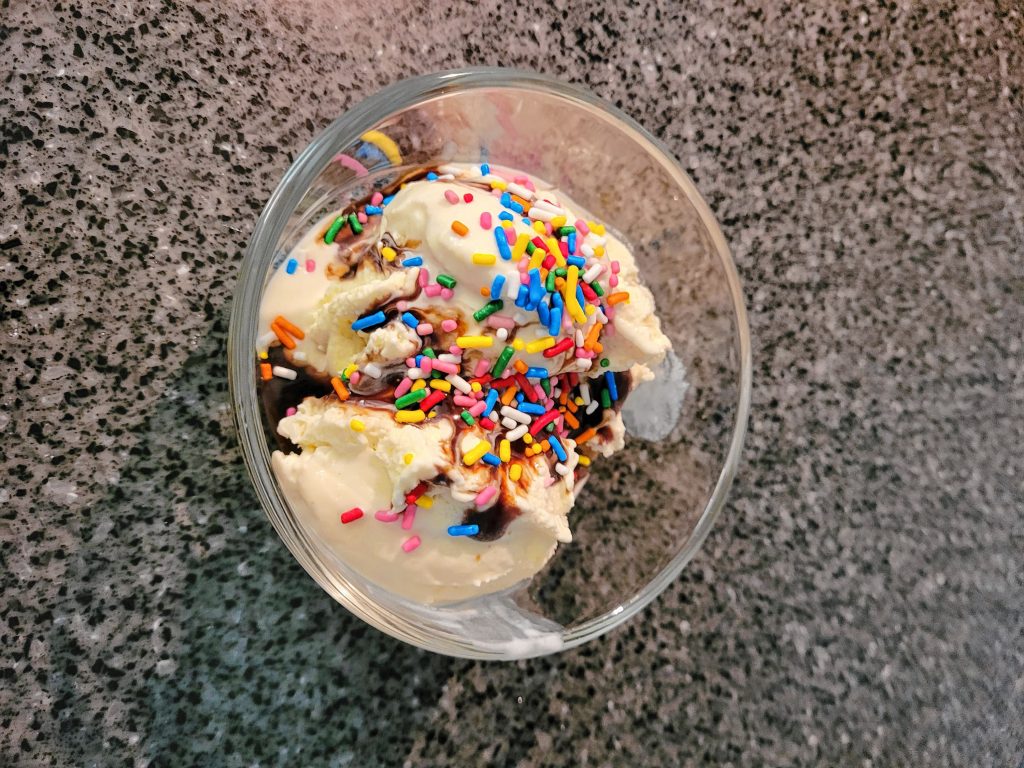 Vanilla dairy ice cream with chocolate sauce and sprinkles.