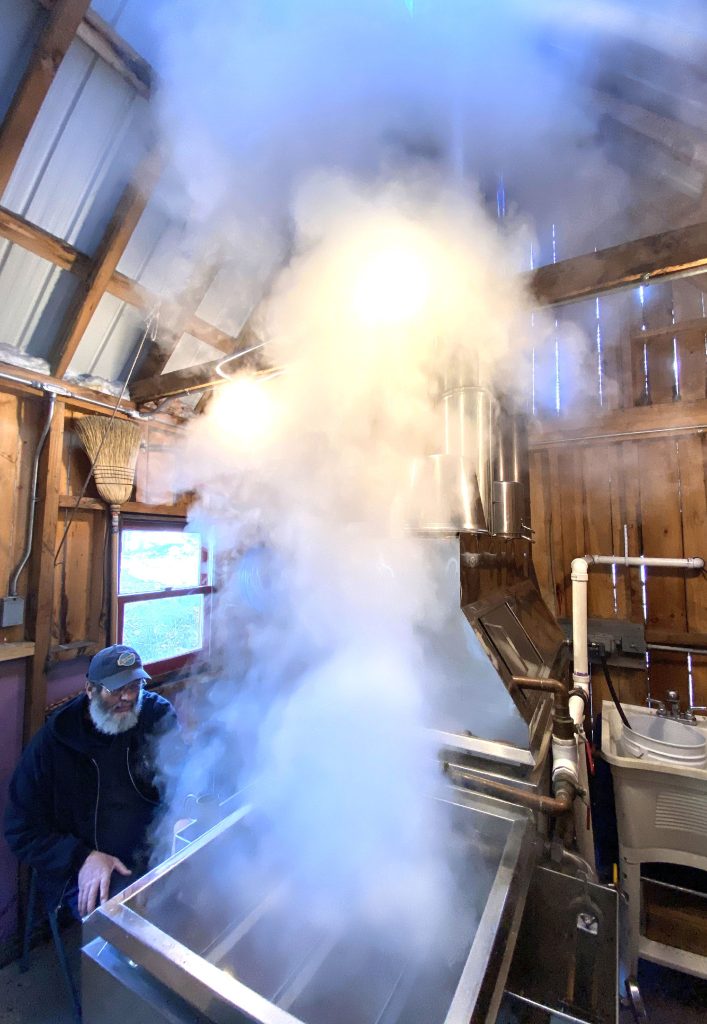 Russell Lampron of Red Roof Maples in Loudon looks at his hydrometer as the steam rises from  his evaporator as he boiled sap at his farm operation on Saturday, March 13,2021. Lampron is retiring after this maple season and moving to North Carolina. GEOFF FORESTER
