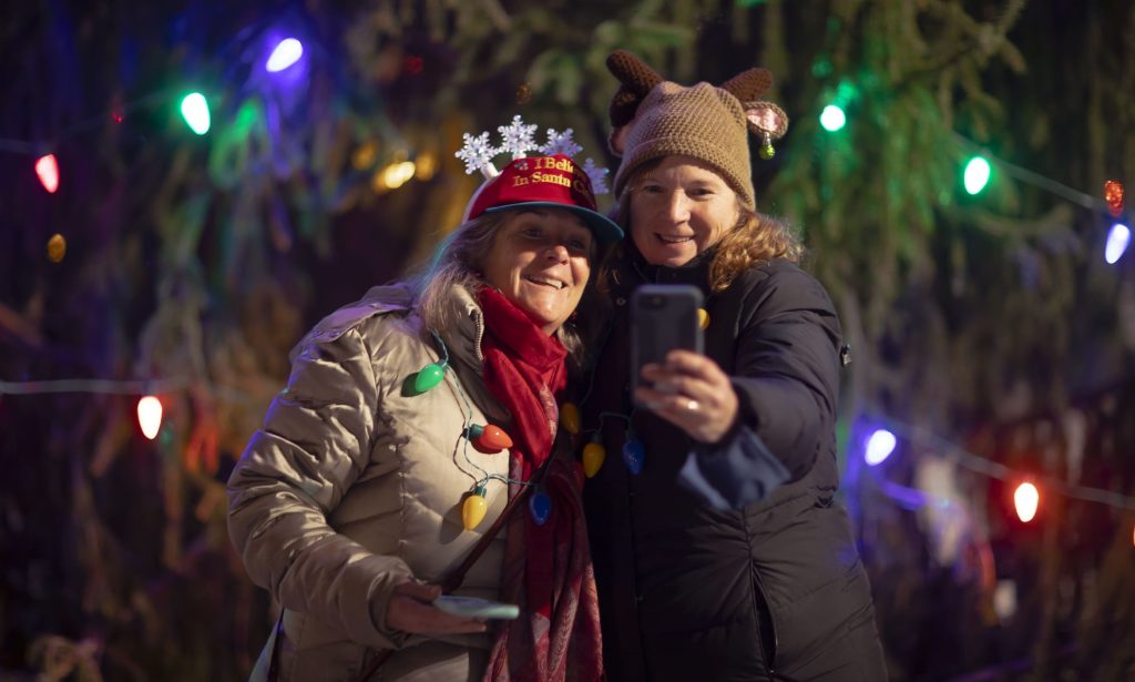 Anne White (left) and Debbie Camejo both from Bridgewater, New Hampshire take a selfie in front of the Christmas tree on City Plaza in front of the State House at the start of Midnight Merriment on Friday night. 