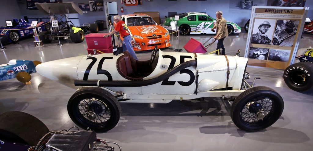 In this Wednesday, May 31, 2017 photograph, volunteers wheel supplies past a 1915 Duesenberg race car (#25), which raced in Boston, at the North East Motor Sports Museum in Loudon, N.H. The museum dedicated to motorsports in New England resides just outside the front gates the New Hampshire Motor Speedway. (AP Photo/Charles Krupa) Charles Krupa