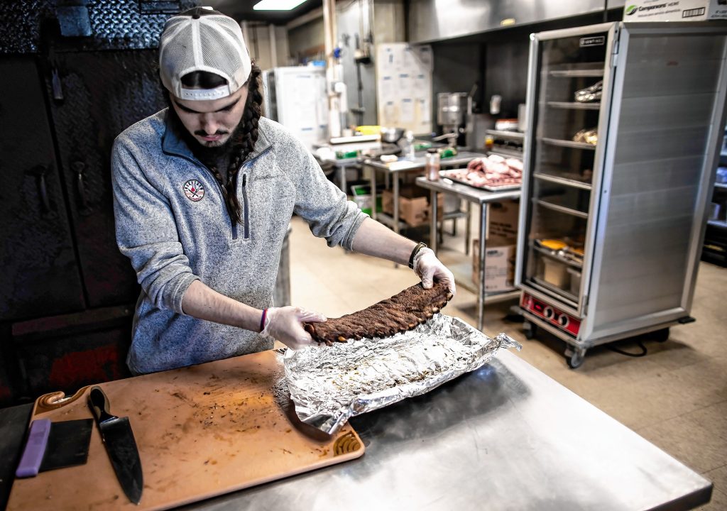 Smokeshow Barbeque manager Andrew Moran gets ready to cut up some ribs at their present location on Ft. Eddy Road in Concord. The eatery will be moving to South Main Street in January. GEOFF FORESTER