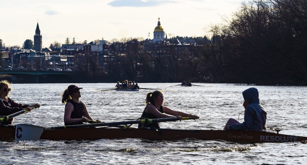 One of the two Concord girls crew boats make their way down the Merrimack River with the Concord skyline in the backround on Tuesday evening, April 5, 2022 on the first time on the water for the season. GEOFF FORESTER